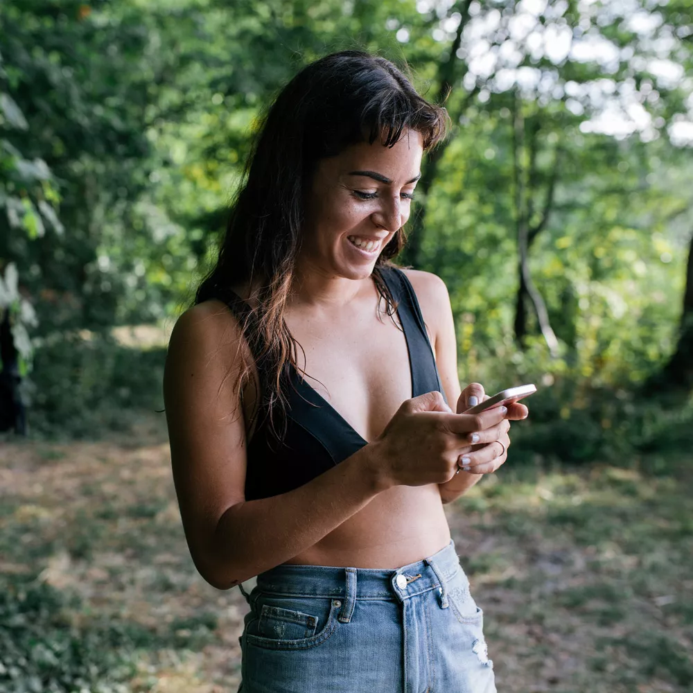 Eine Frau steht im Wald und schaut auf ihr Smartphone.