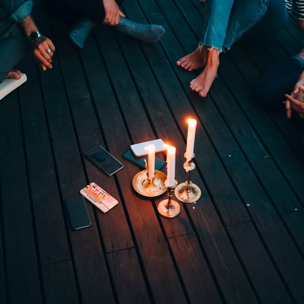 Eine Gruppe von Menschen sitzt um Kerzen herum, in der Mitte liegen ihre Smartphones.